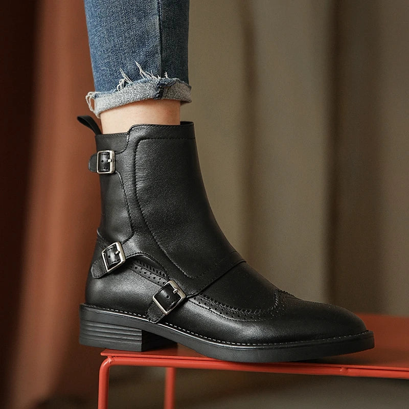 Woman wearing black leather Chelsea boot with buckle straps, standing on red stool