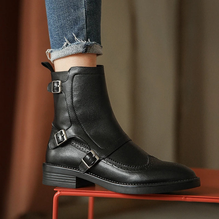 Woman wearing black leather Chelsea boot with buckle straps, standing on red stool