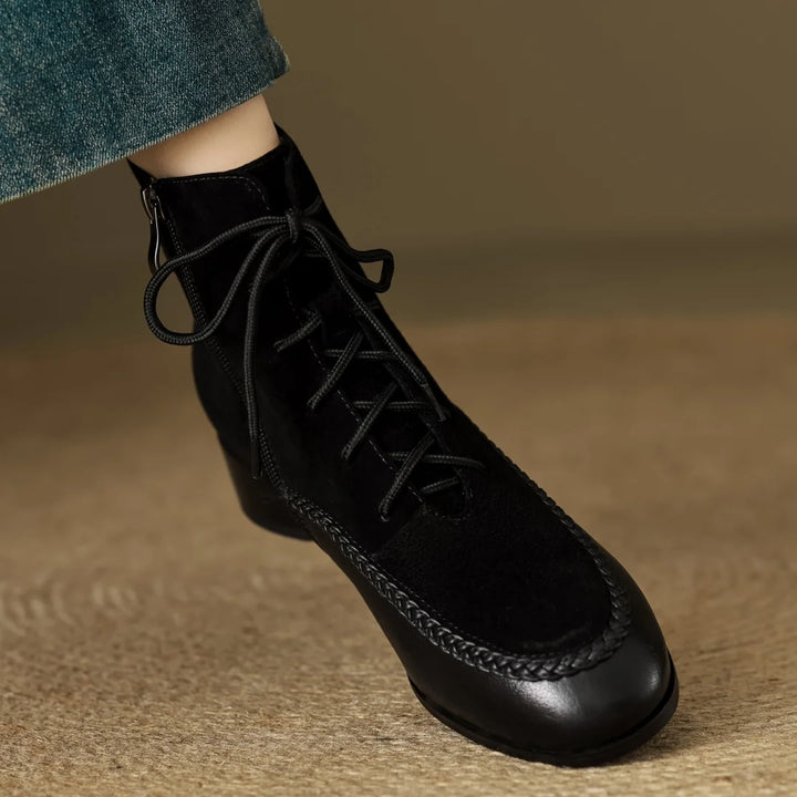 Black suede ankle boot with braided leather toe trim on foot