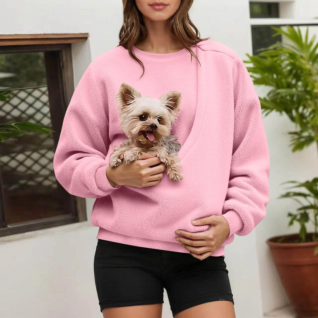 Woman holding small dog in pink fleece pullover pocket outdoors