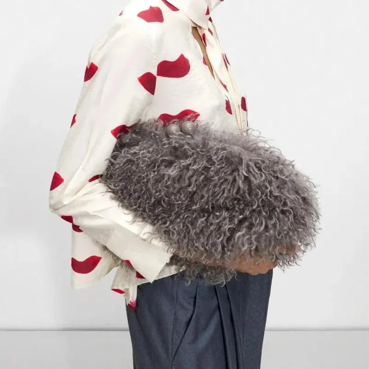 Model carrying a dark grey curly faux fur clutch bag under her arm