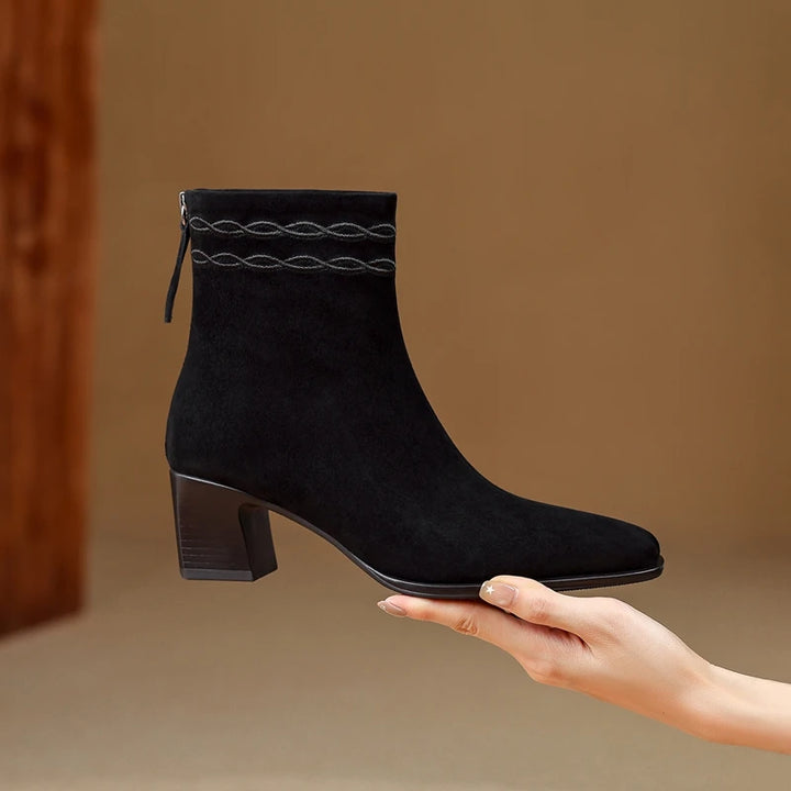 Black suede ankle boot held in hand showing side profile