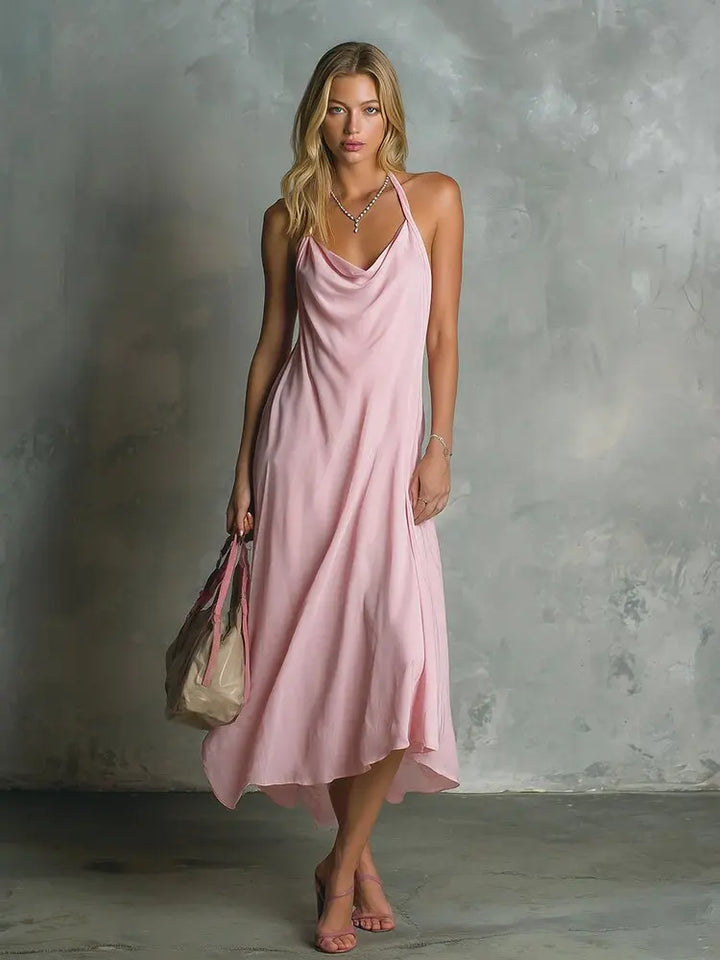 Woman in pink cowl neck halter midi dress standing against textured wall