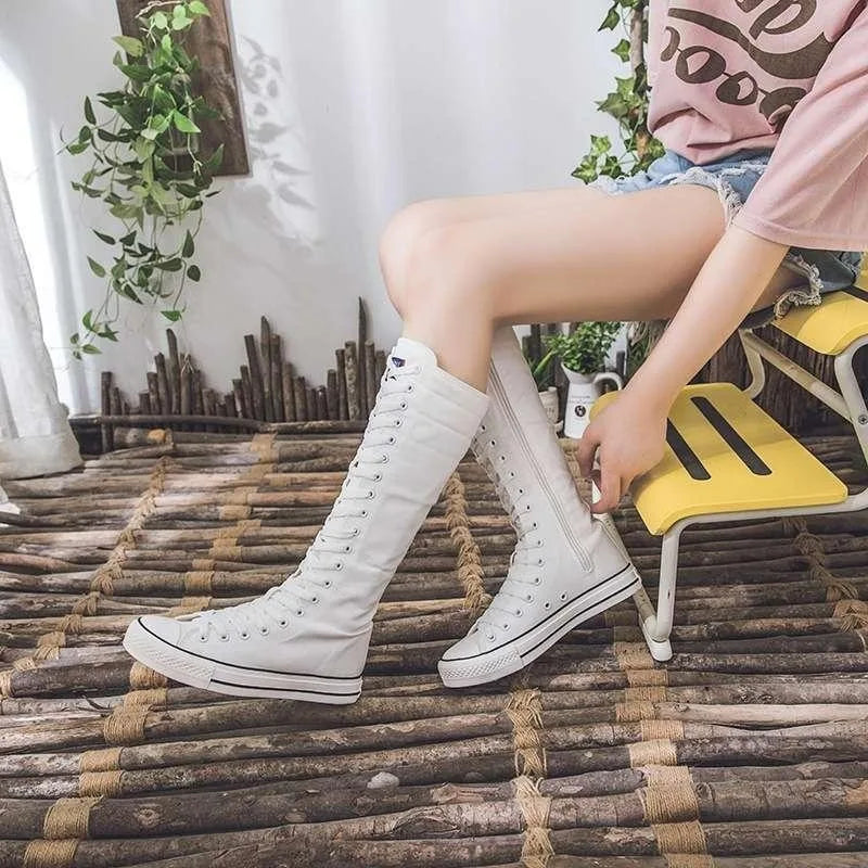 Model sitting wearing white knee-high lace-up canvas boots