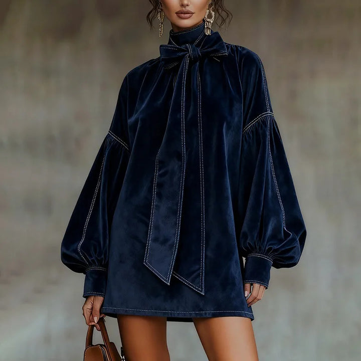 Woman wearing navy velvet mini dress with bow tie collar and lantern sleeves, front view close up