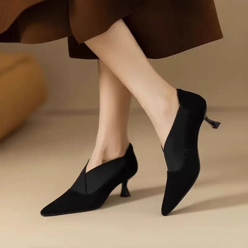Black suede kitten heel pumps worn while walking, angled view