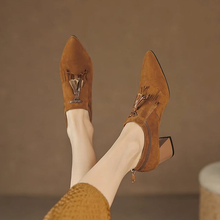 Model kicking up feet wearing brown suede pumps with tassel detail