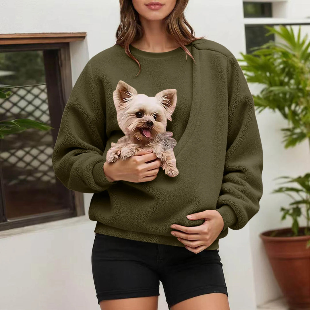 Woman holding small dog in olive green fleece pullover pocket outdoors
