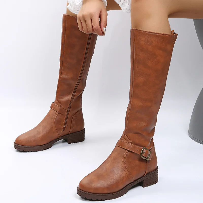 Model seated wearing brown knee-high boots with buckle detail