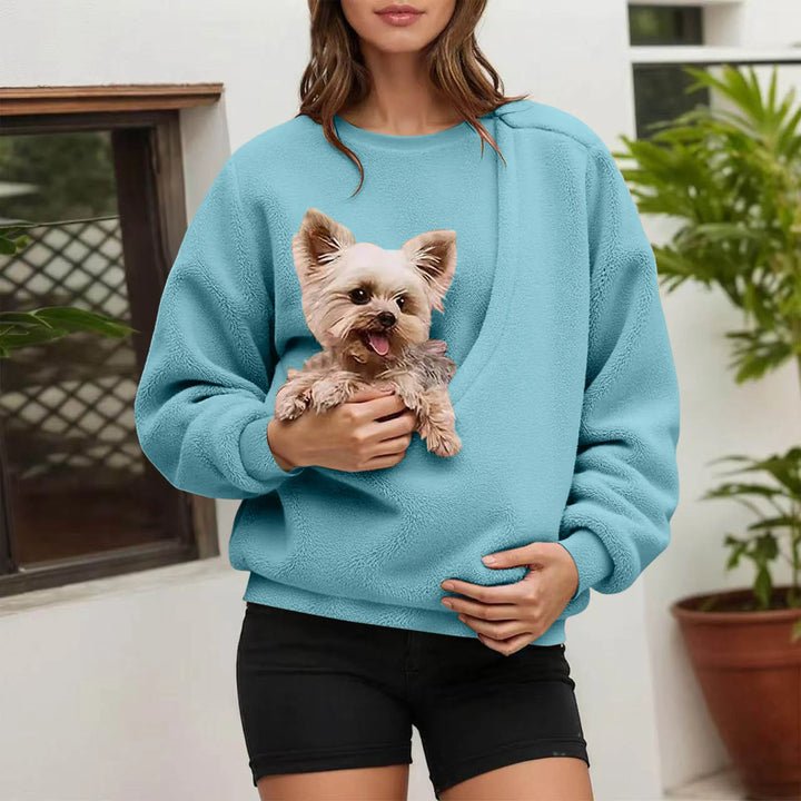 Woman holding small dog in sky blue fleece pullover pocket outdoors