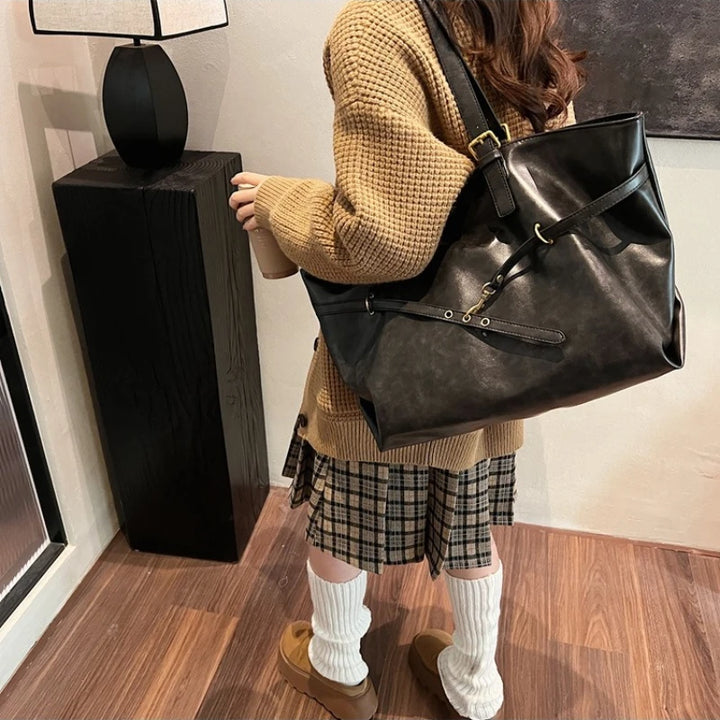 Woman carrying black leather tote bag with plaid skirt