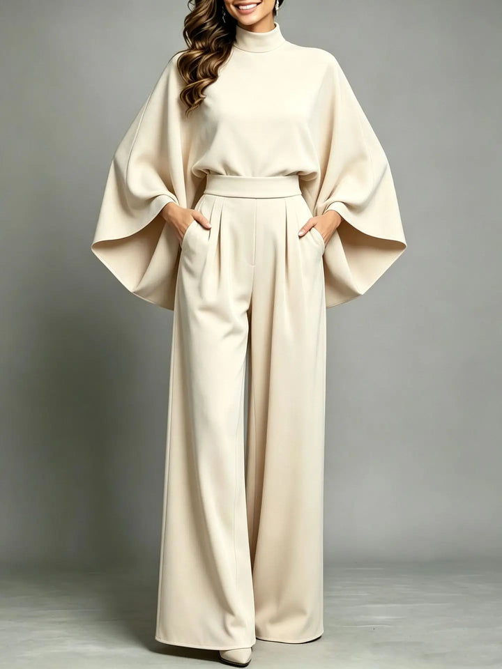 Front view of cream cape sleeve top and pleated wide leg trousers with hands in pockets