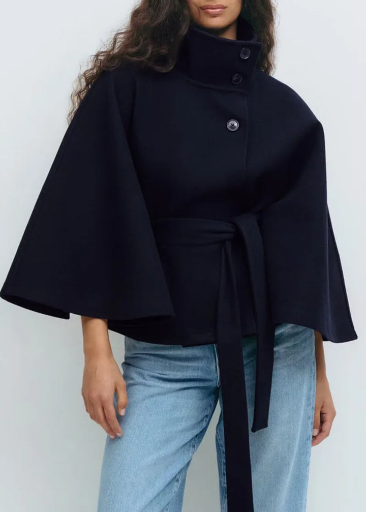 Woman wearing navy cape jacket with belted waist, front view