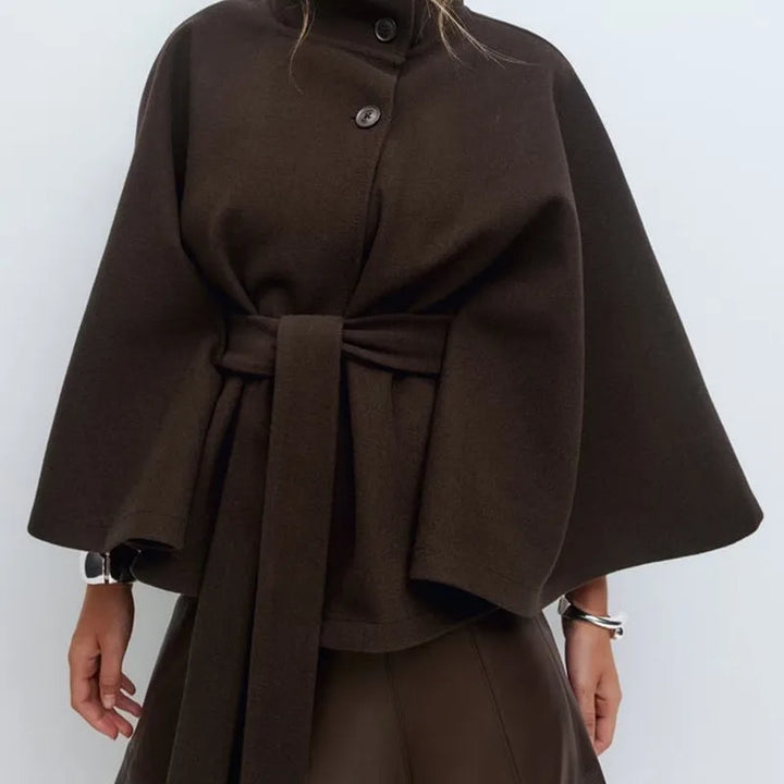 Woman wearing dark brown cape jacket with belted waist, front view