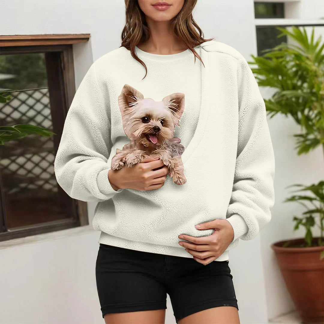 Woman holding small dog in cream fleece pullover pocket outdoors