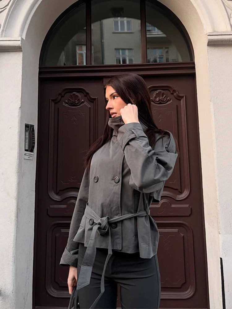 Side view of woman wearing grey cropped trench coat with tie belt