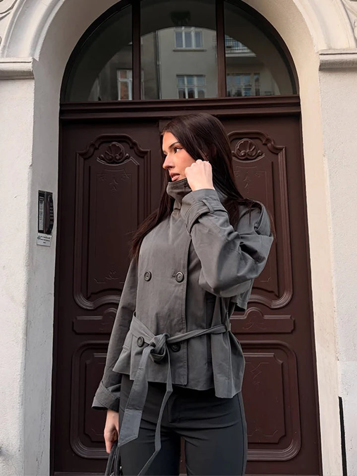Side view of woman wearing grey cropped trench coat with tie belt