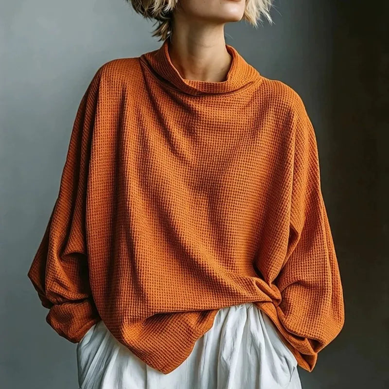 Woman wearing orange waffle knit top with funnel collar, front view