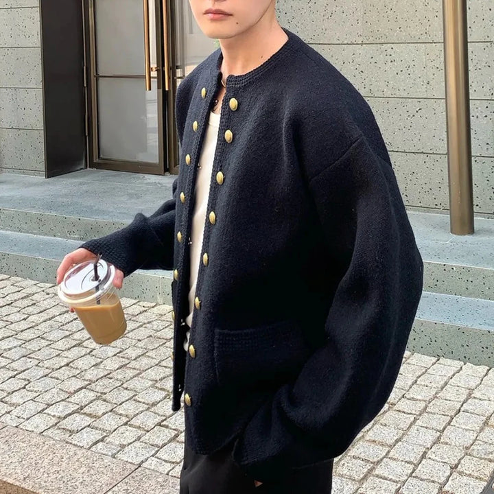 Man wearing black double breasted knit cardigan holding coffee, side view