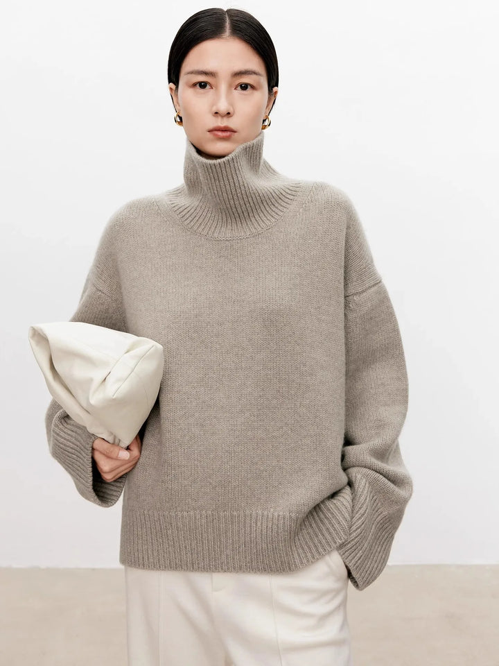 Front view of taupe cashmere turtleneck sweater with leather bag