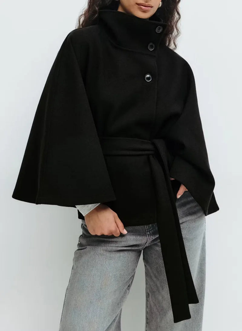 Woman wearing black cape jacket with belted waist and stand collar