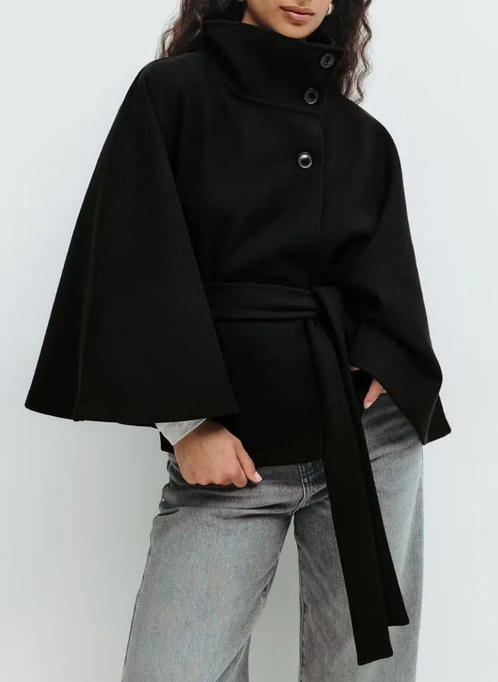 Woman wearing black cape jacket with belted waist and stand collar