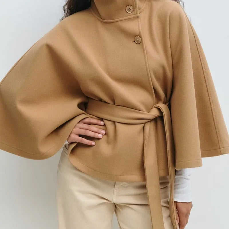 Woman wearing camel cape jacket with belted waist and stand collar, front view