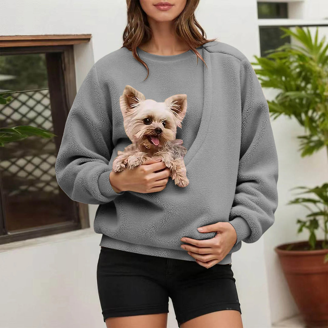 Woman holding small dog in grey fleece pullover pocket outdoors