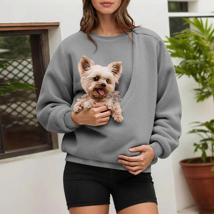 Woman holding small dog in grey fleece pullover pocket outdoors